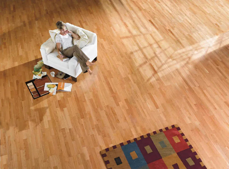 Looking down on a cherry strip floor in a large room, with a woman reading in a white armchair.