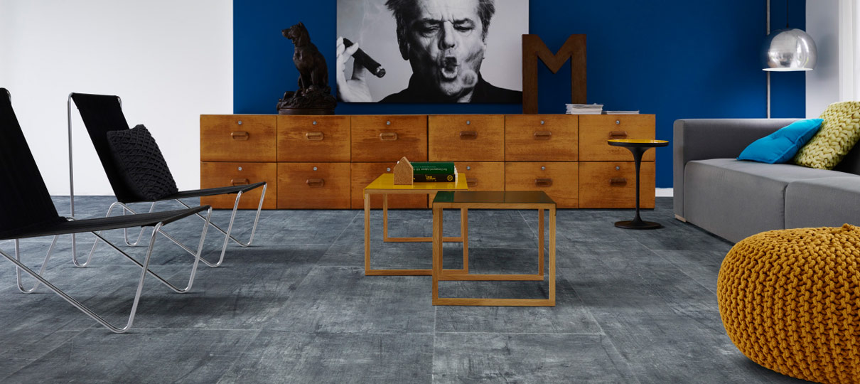 Weathered grey tile-effect flooring in a living room with a blue feature wall and a bank of wooden drawers.