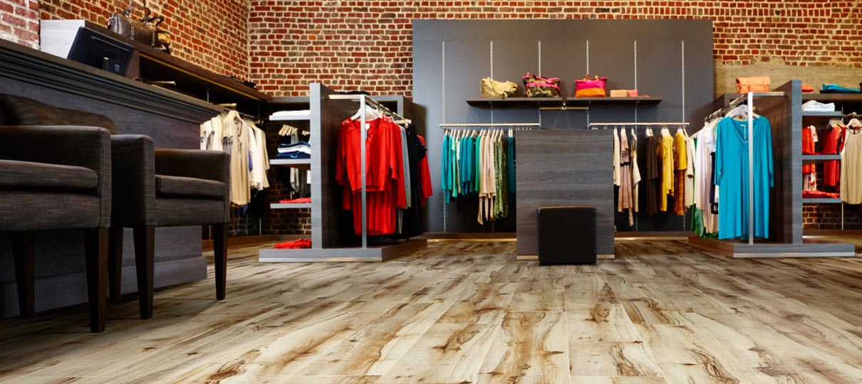 Figured light wood-effect planks across a clothes shop floor, with exposed brick walls and hanging rails.