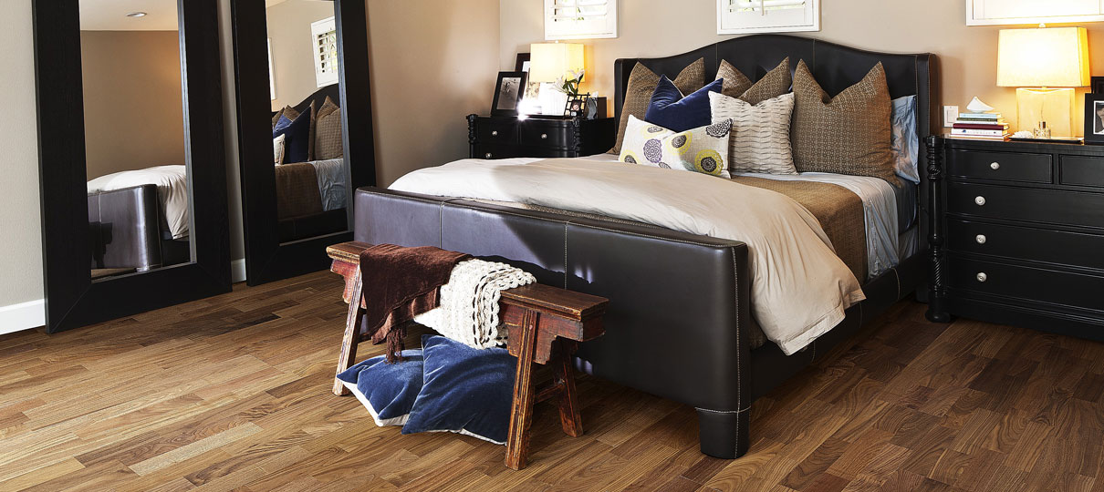Mid-brown walnut plank flooring in a bedroom with a dark leather bed and tall mirrors.