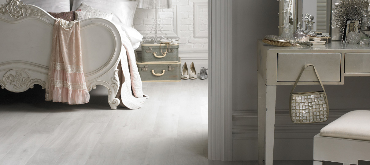 Whitewashed wood-effect flooring running from a bedroom into a dressing area, with a cream French bed.