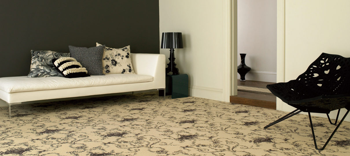 Cream carpet with a dark trailing floral pattern in a sitting room, with a white daybed against a charcoal wall.